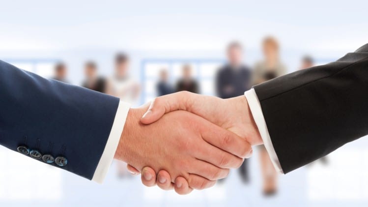 Two hands of businessmen shaking with other people blurred in the background